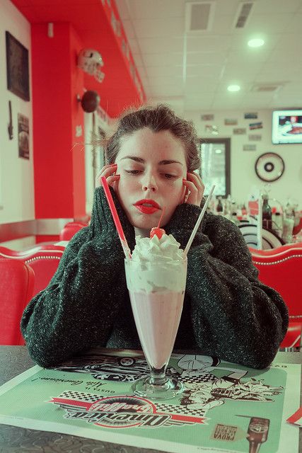 a woman sitting at a table with a milkshake in front of her face