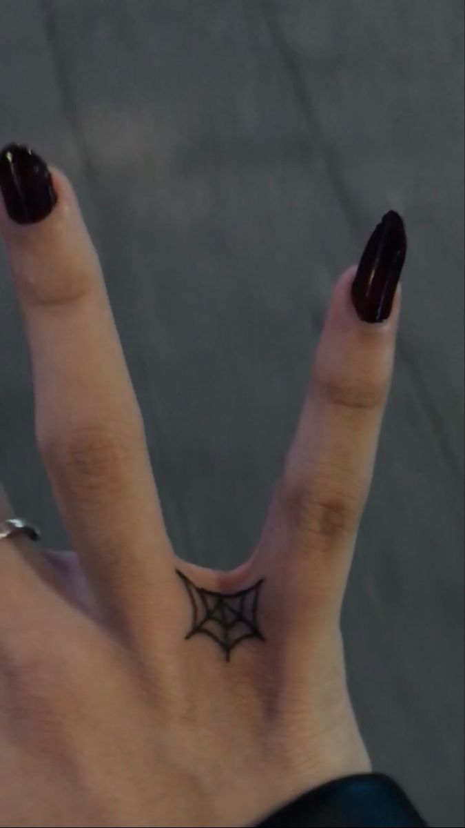 a woman's hand with a black spider web tattoo on her thumb and finger