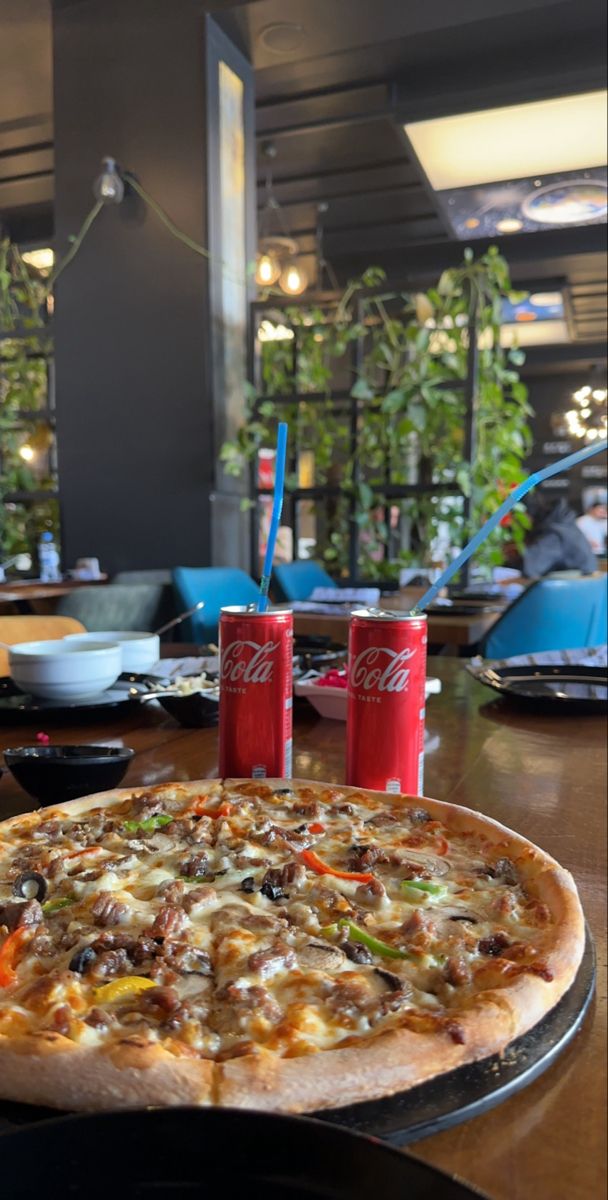 a pizza sitting on top of a table next to two sodas