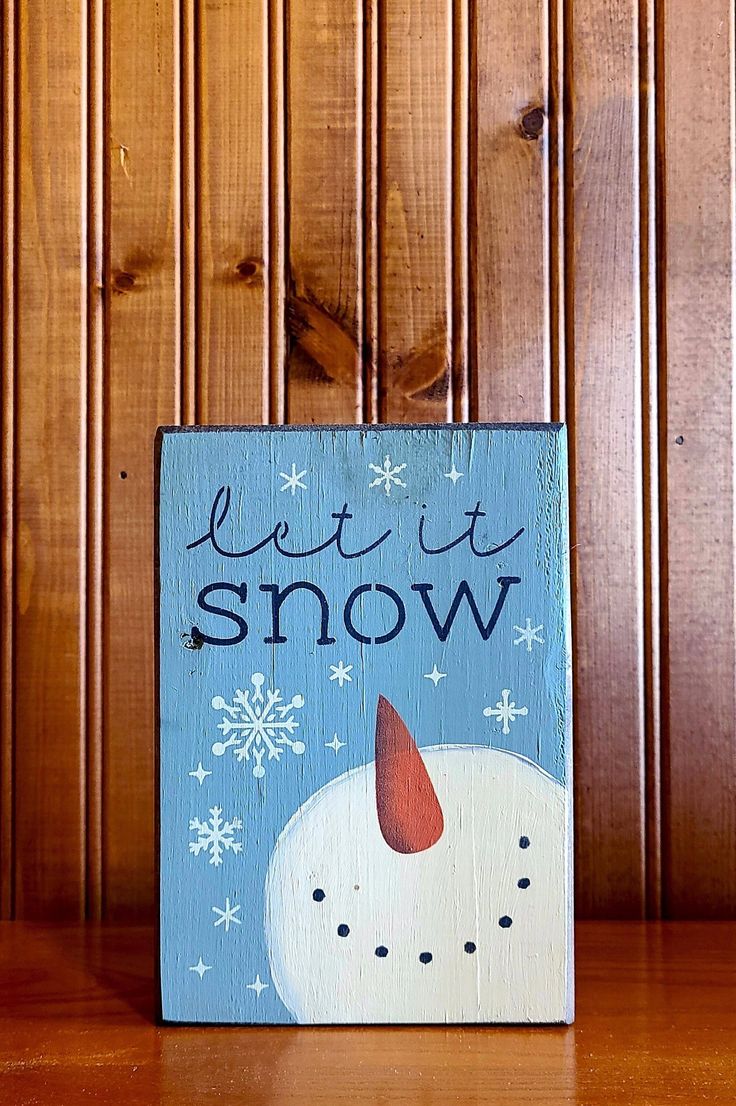 a wooden sign with the words let it snow written on it and an image of a snowman