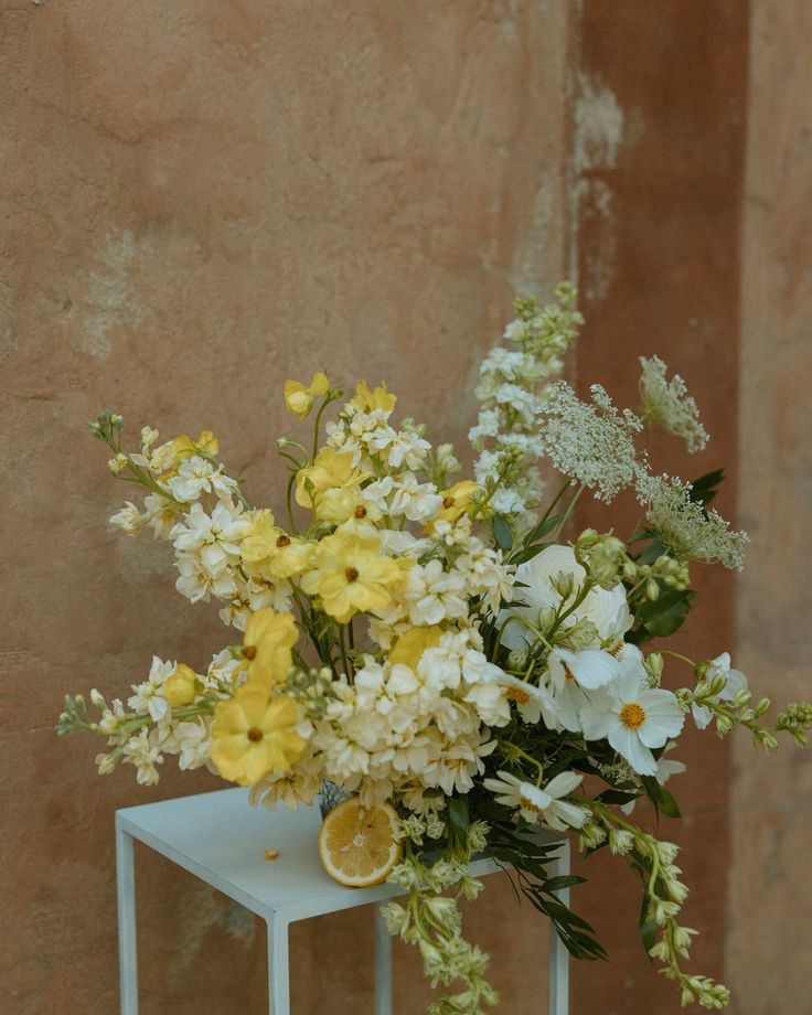 a vase filled with yellow and white flowers on top of a small table next to a wall