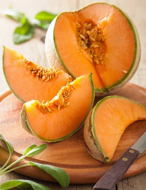 two pieces of melon on a wooden cutting board with a knife and green leaves