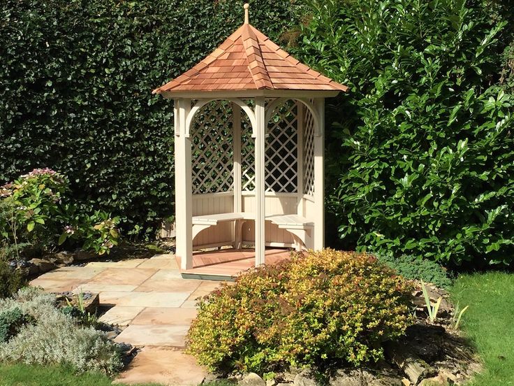 a white gazebo sitting in the middle of a garden next to bushes and shrubbery