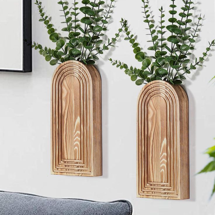 two wooden vases with plants in them on a wall next to a gray couch