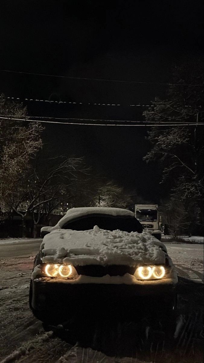 a car is parked in the snow with its headlights turned on and it's headlamps glowing