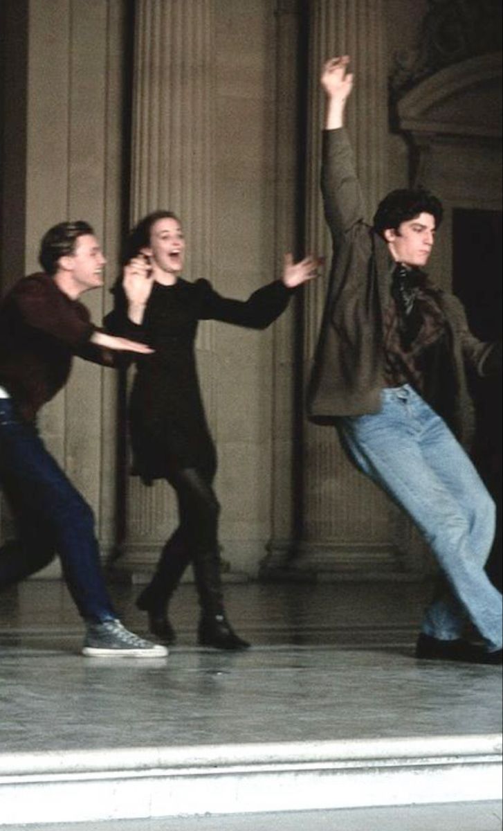 three men are dancing on the street in front of a building with columns and pillars