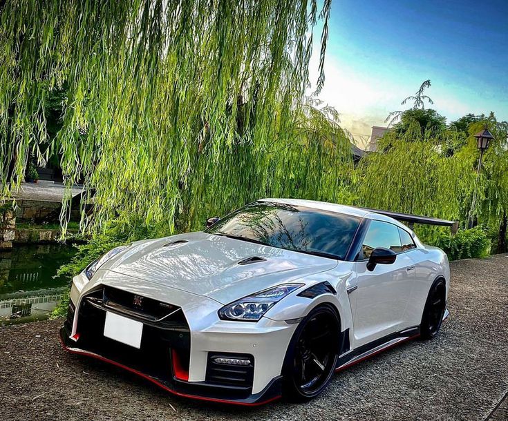 a white nissan sports car parked in front of a tree with green leaves on it