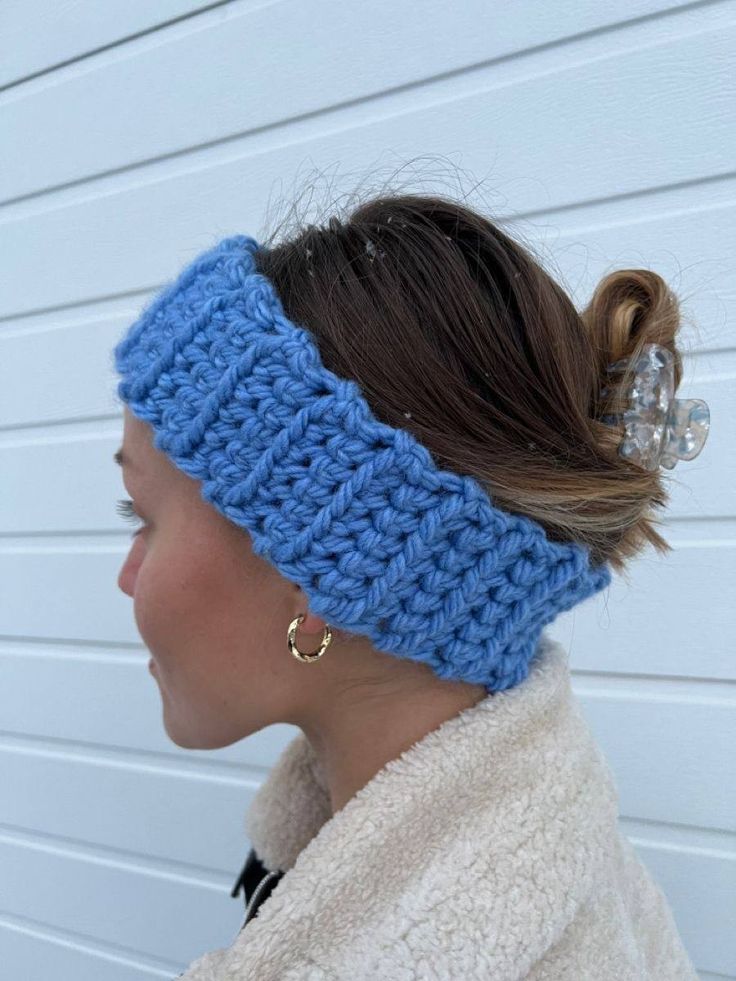 a woman wearing a blue crochet headband with a ponytail in front of a white wall