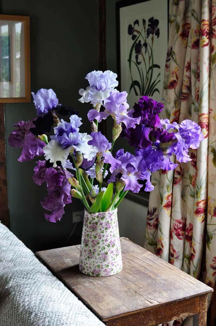 a vase filled with purple and white flowers on top of a wooden table next to a window