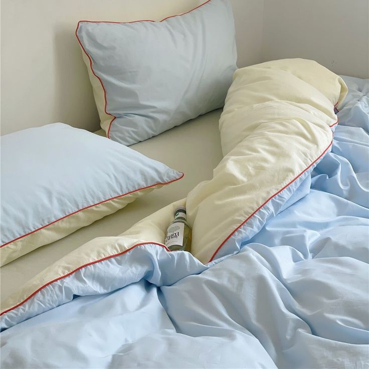 a bed with blue sheets and pillows on top of it, next to a bottle of beer