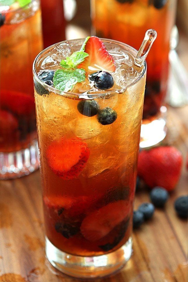 two glasses filled with fruit and ice sitting on top of a wooden table next to strawberries