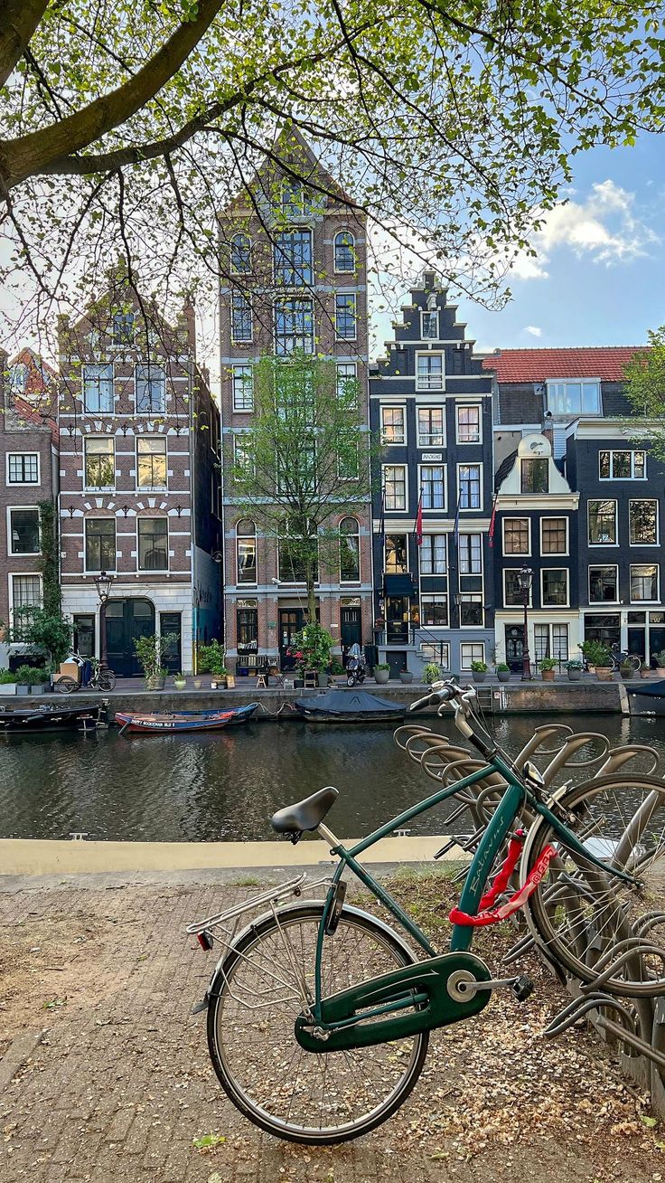 two bikes parked next to each other on the side of a river with buildings in the background