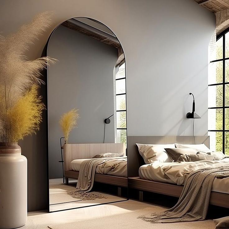 a large bed sitting under a tall mirror next to a vase with dry grass in it