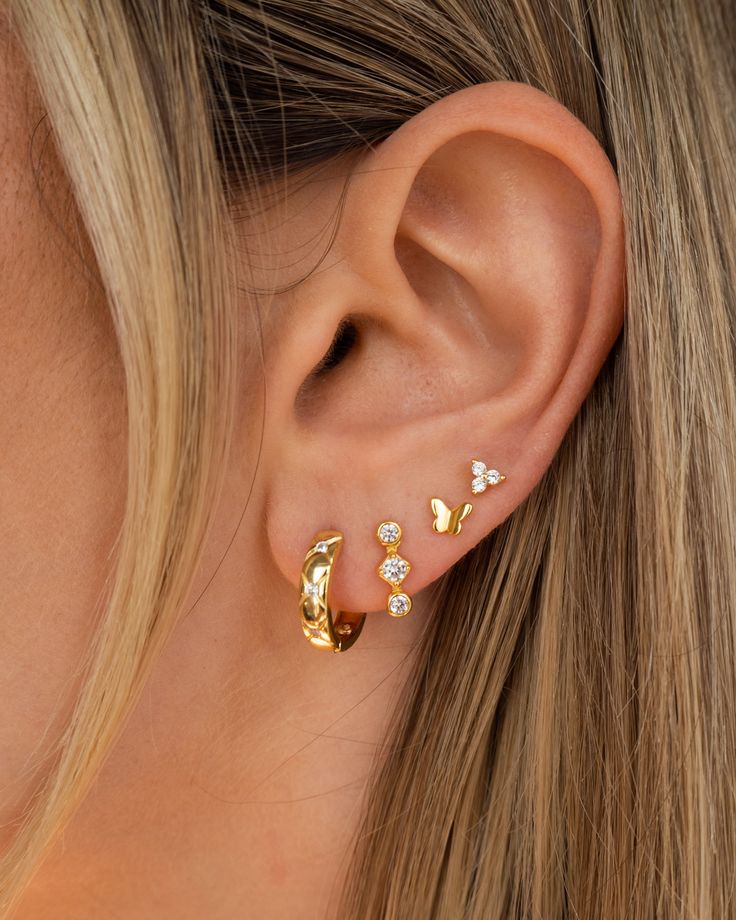 a close up of a woman's ear with three small gold earrings on it