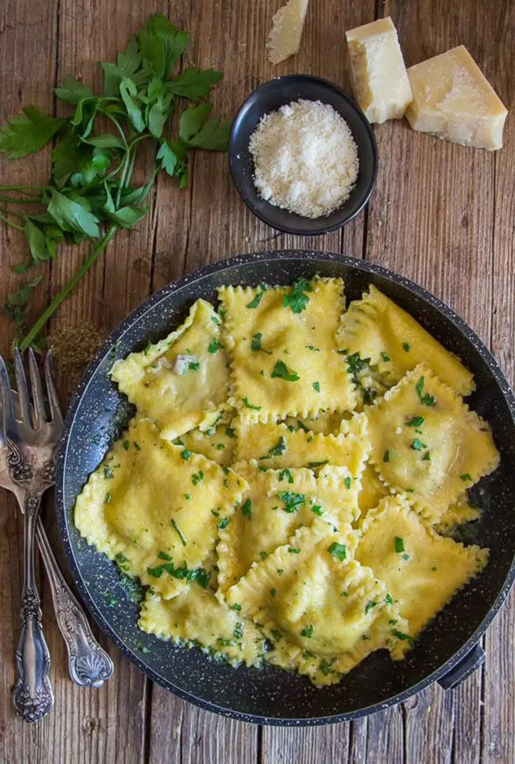 a plate of ravioli with parmesan cheese and herbs next to it on a wooden table