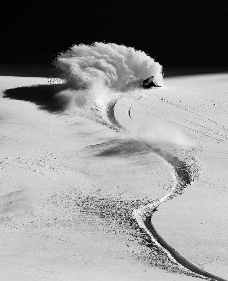 a person riding skis down a snow covered slope in the mountains with spray coming out of it