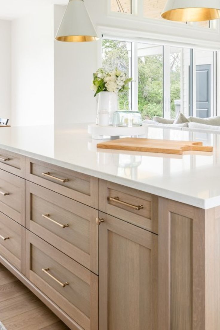 a large kitchen with white counter tops and wooden cabinets in front of a big window