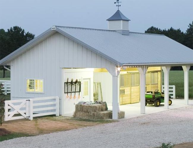 a white barn with a horse and tractor parked in the driveway next to it at dusk