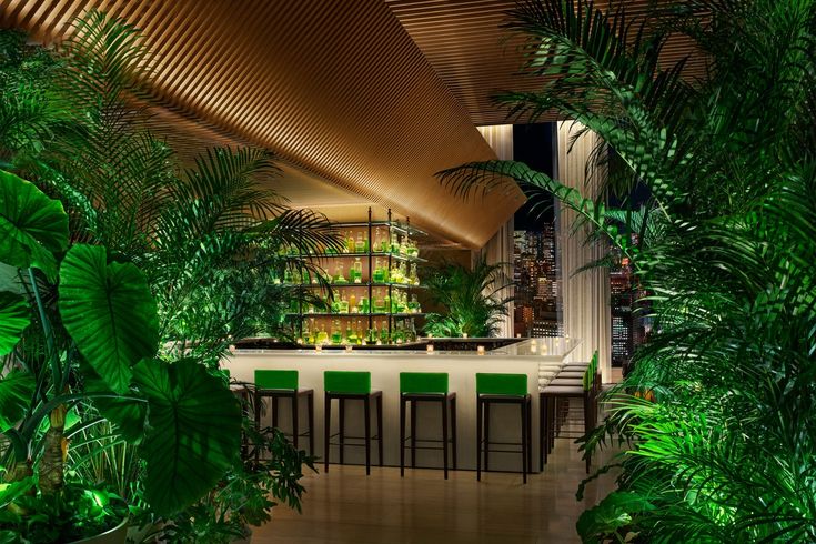 the interior of a tropical restaurant with green chairs and greenery on the walls, along with an indoor bar