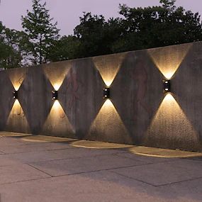 a wall with several lights on it next to a sidewalk and trees in the background