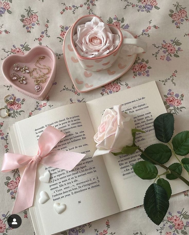 an open book on a table next to a rose and a heart shaped trinket