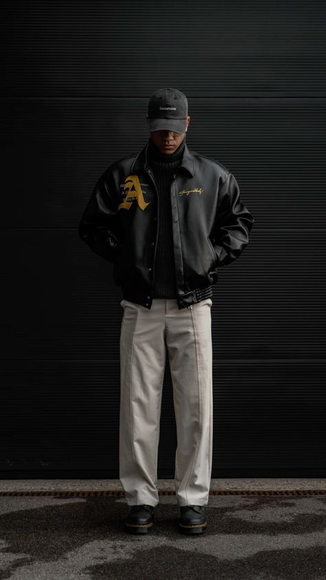 a man standing in front of a garage door wearing a black jacket and khaki pants