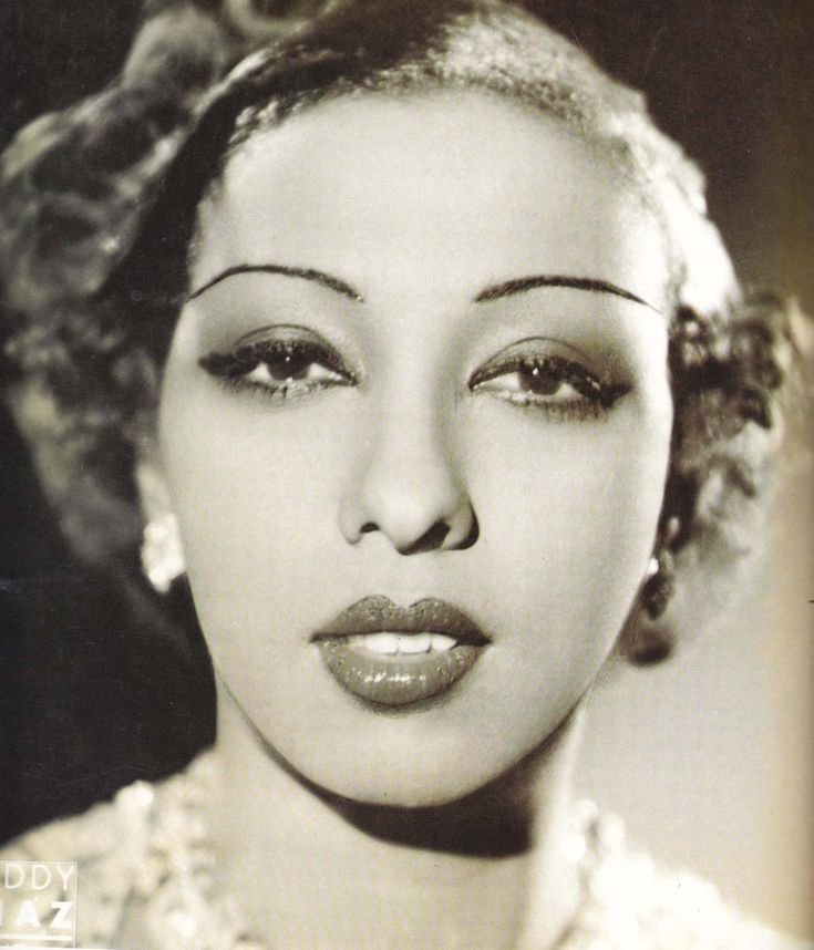 a black and white photo of a woman with curly hair wearing an evening dress, necklace and earrings