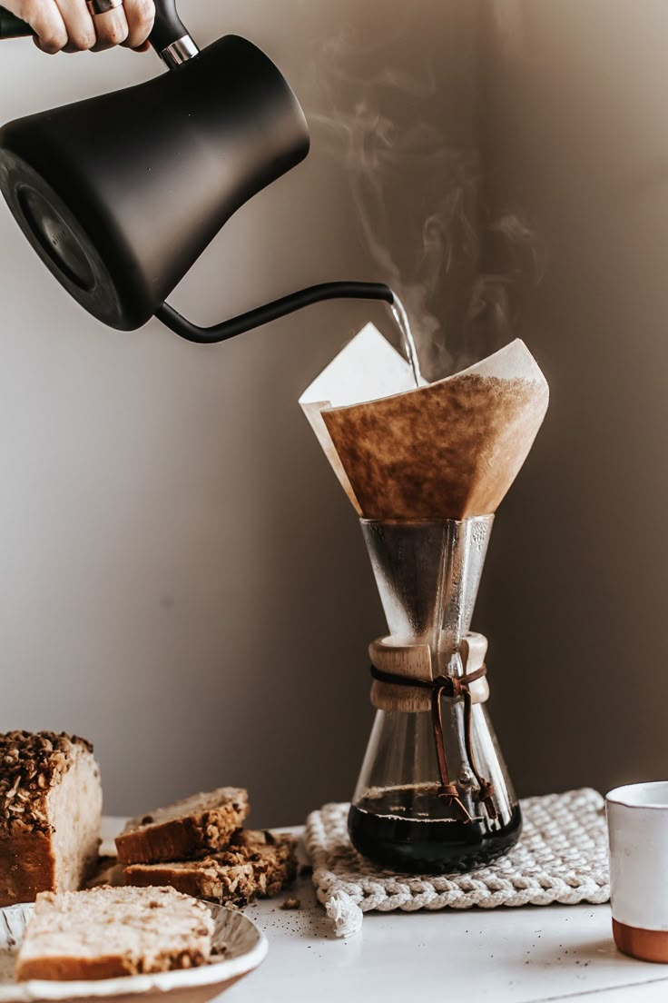 a person pouring coffee into a cup on top of a table next to sliced bread