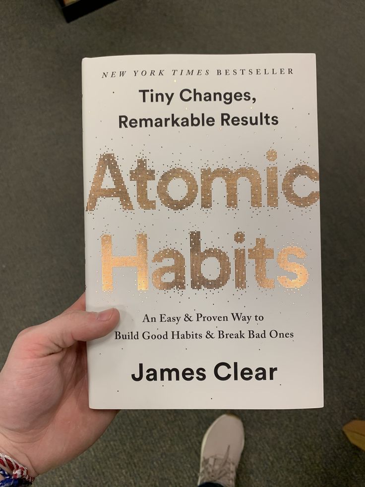 a person holding up a book with the title atomic habitts written in gold on it