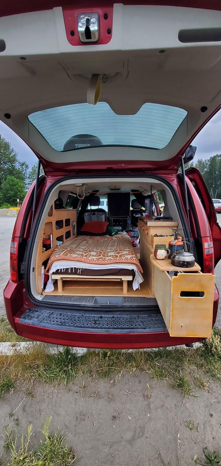 the back end of a red car with its hatch open and bed in it's trunk