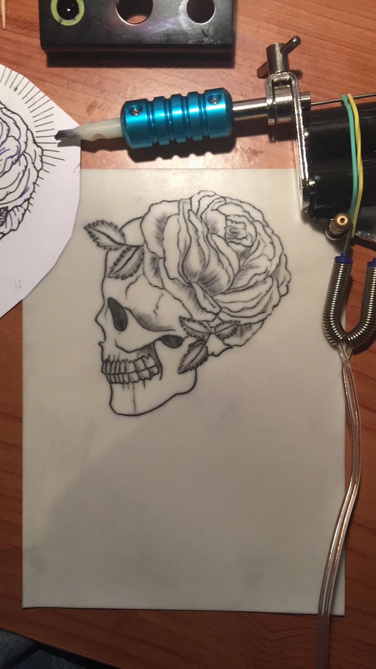 a tattoo machine with a skull and rose on it next to a piece of paper