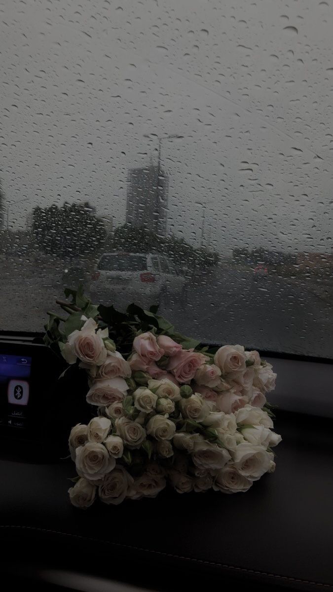 flowers are sitting on the dashboard of a car in the rain, next to a digital clock