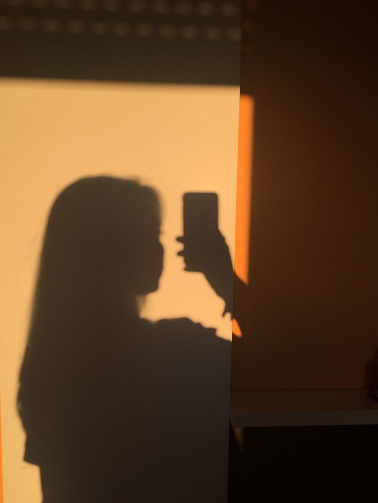 the shadow of a person holding a cell phone in front of a wall with a light shining on it