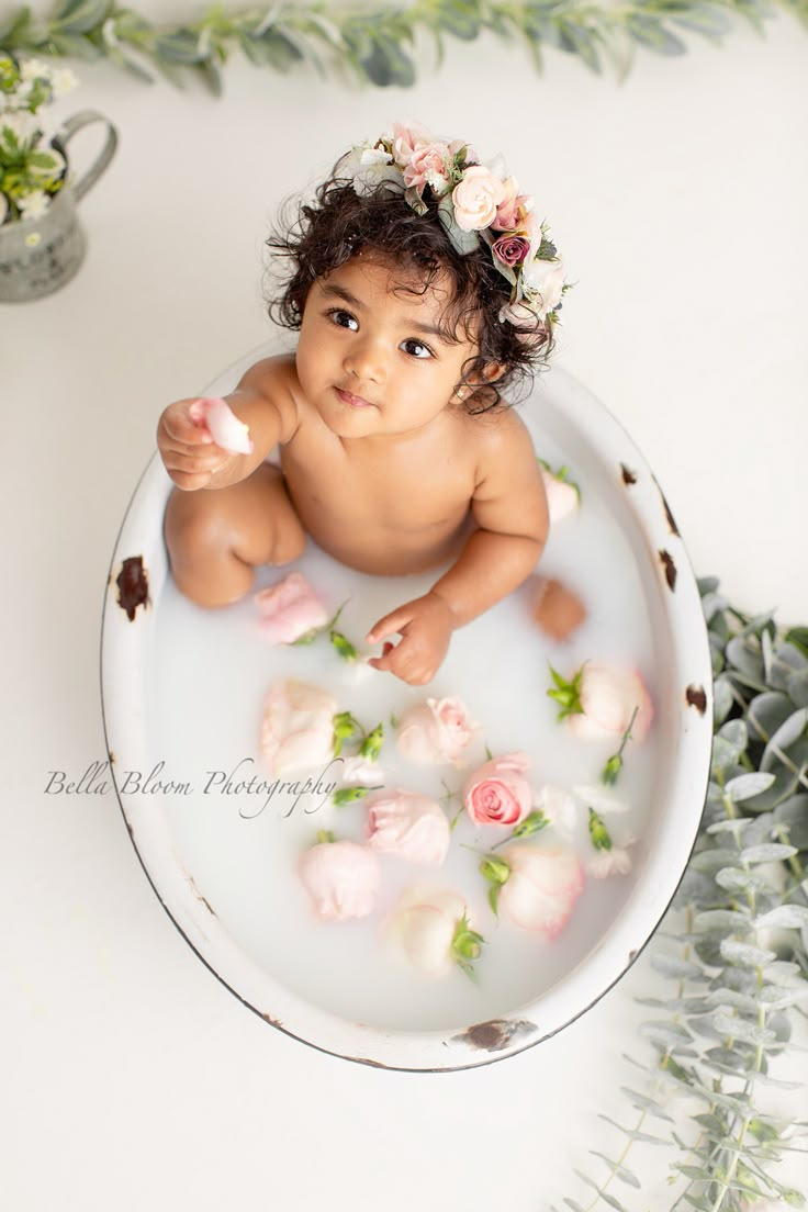 a baby sitting in a bathtub with flowers on it's head, surrounded by greenery