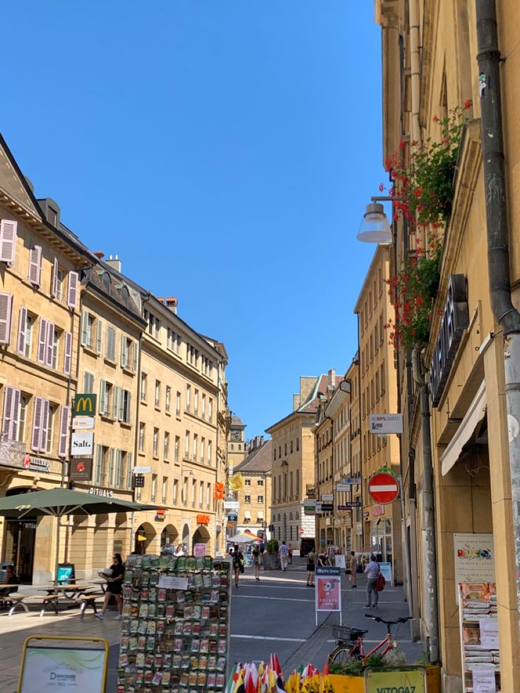 an empty city street lined with buildings and flowers on the sidewalk, surrounded by shops