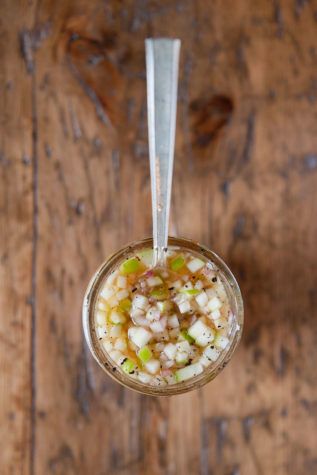 a glass jar filled with food sitting on top of a wooden table next to a spoon