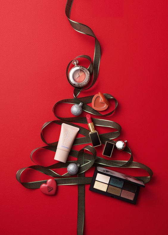 a christmas tree made out of makeup and other items on a red background with a ribbon