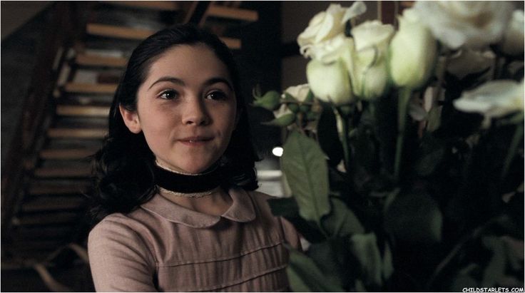 a woman standing next to a bunch of flowers in front of a vase filled with white roses