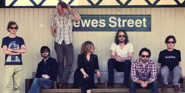 a group of people sitting on top of a bench under a train station sign that reads ewes street