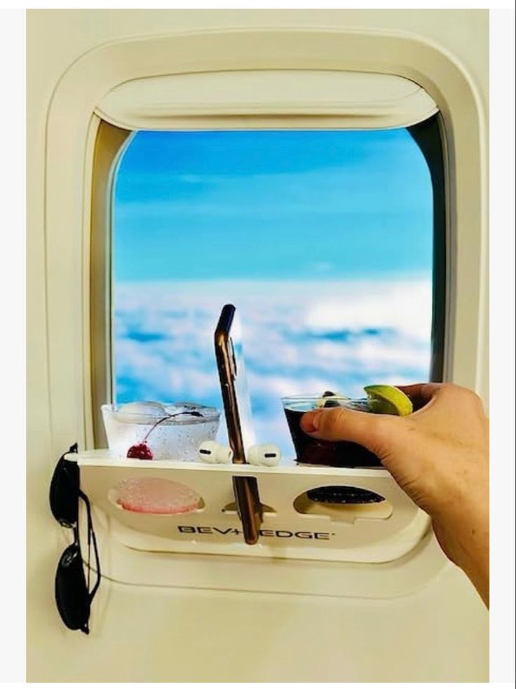 a hand is holding a tray with food on it in front of an airplane window