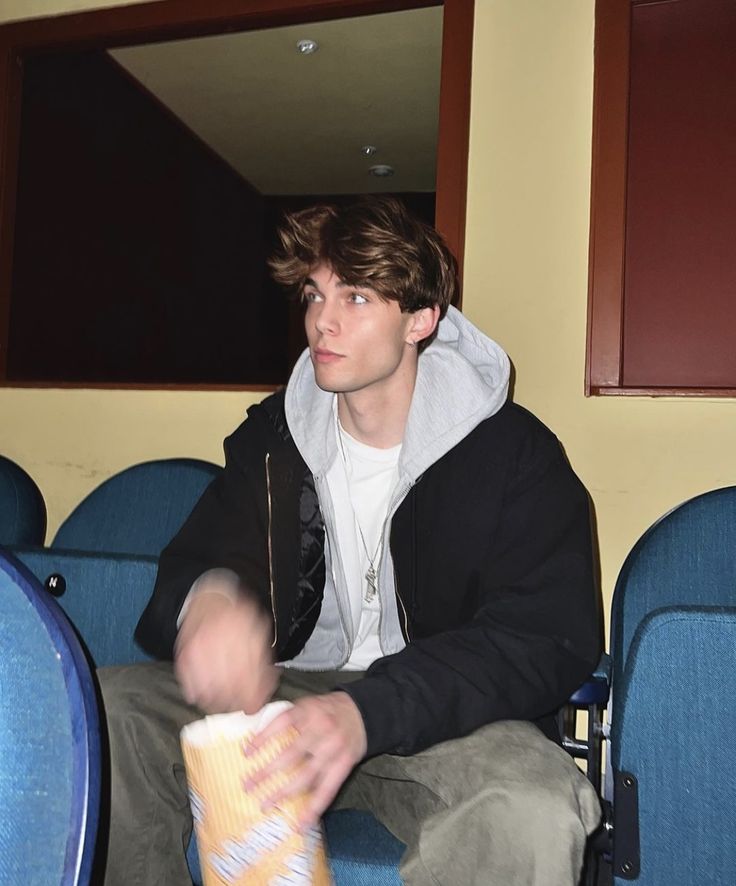 a young man sitting in a stadium holding a bag of popcorn