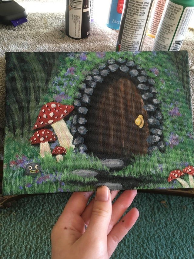 someone is holding up a painting with mushrooms in the grass and flowers on it,