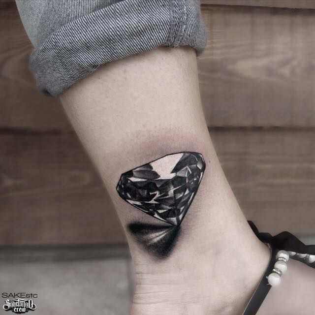 a black and white diamond tattoo on the left side of the ankle, with an abstract design