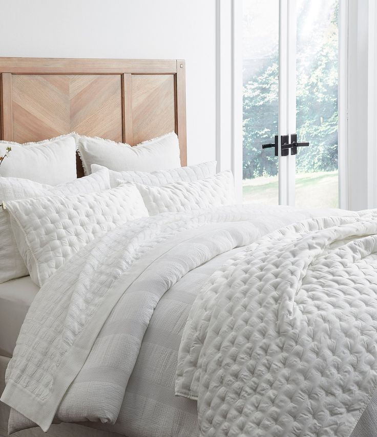 a bed with white comforters and pillows in a bedroom next to a large window