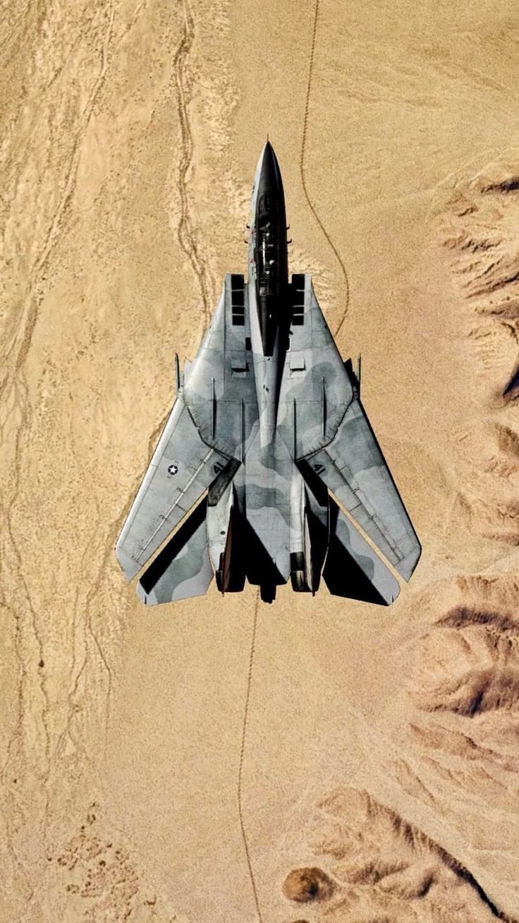 a fighter jet flying through the air over sand and desert terrain in an aerial view