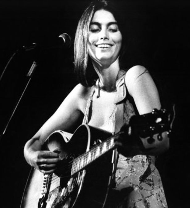 a woman holding a guitar while standing in front of a microphone