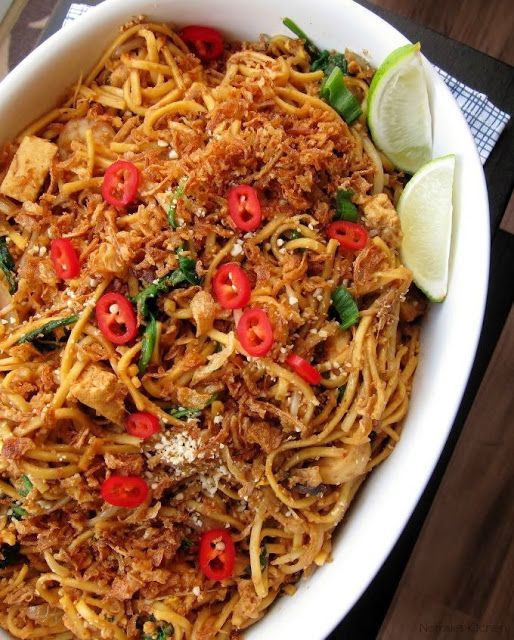 a white bowl filled with noodles and vegetables on top of a wooden table next to a lime wedge