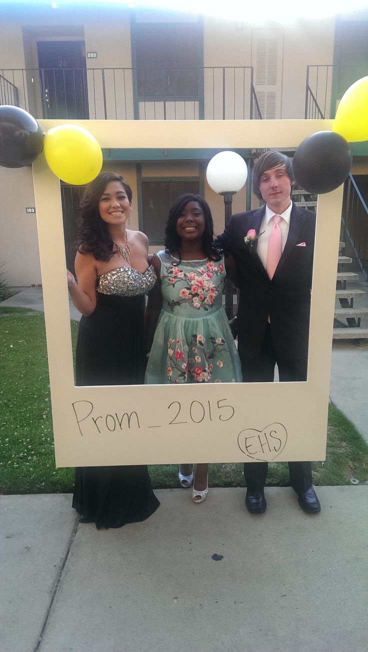 two women and a man are posing for a photo in front of a sign that says prom