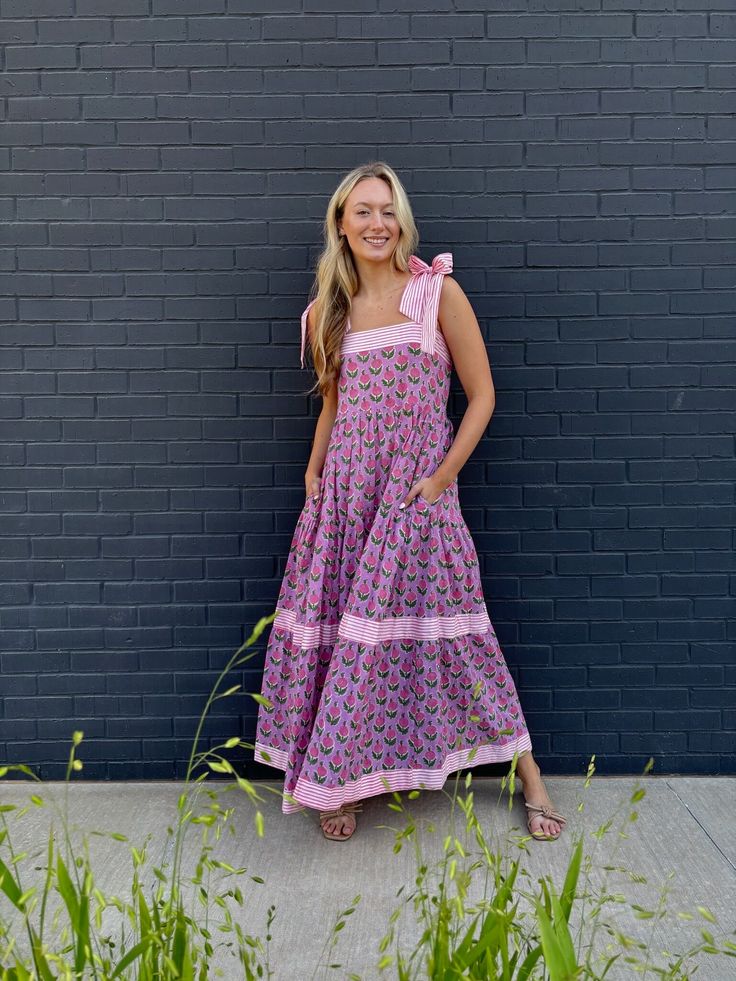 Meet Maisie, our newest cotton block print maxi dress in a Pink Posey print! She's full of sweet details like a tiered skirt, and contrasting striped banding. The bow straps are adjustable for the perfect fit, and it features a smocked back panel for comfort. Did we mention it has POCKETS!? Whether you're sipping lemonade on the porch or hitting up a summer wedding or soirée, this dress is a fun, versatile addition to your closet. Throw it on with sneakers or sandals, it's truly a go anywhere dr Tiered Cotton Maxi Dress For Garden Party, Cotton Dress With Tie Straps And Tiered Skirt, Cotton Tiered Skirt Maxi Dress For Garden Party, Cotton Tiered Maxi Dress For Garden Party, Cotton Maxi Dress With Tiered Skirt For Garden Party, Cotton Maxi Dress With Tie Straps, Cute Church Dresses, Pink And Blue Dress, Bow Straps