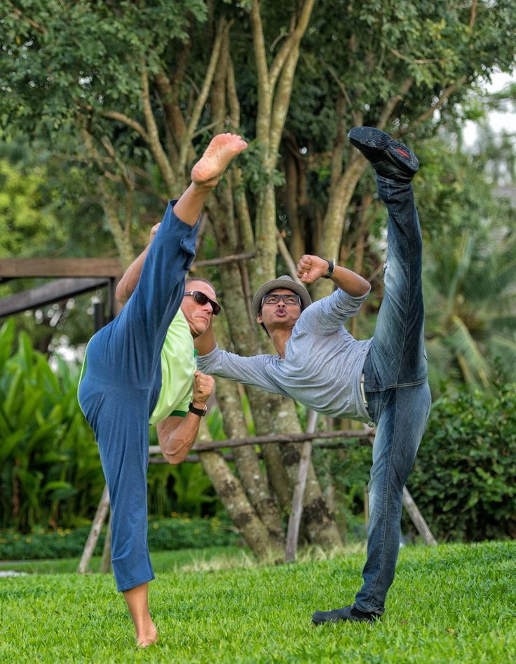 two men doing yoga on the grass in front of some trees and bushes with their hands up